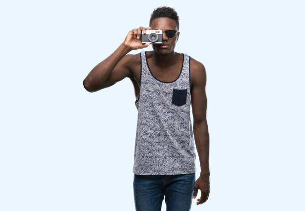 istock Young african american man holding vintage camera with a confident expression on smart face thinking serious 1042737996