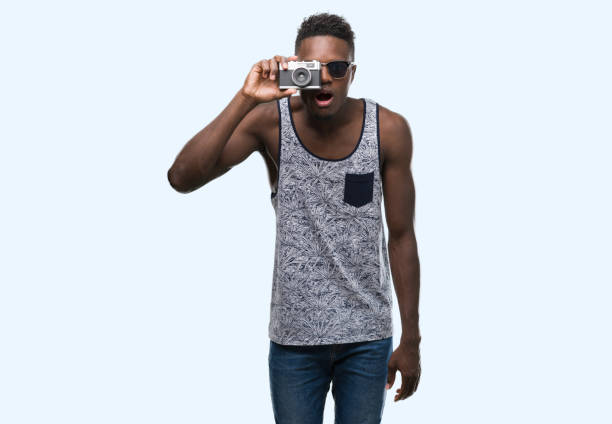 istock Young african american man holding vintage camera scared in shock with a surprise face, afraid and excited with fear expression 1042738010