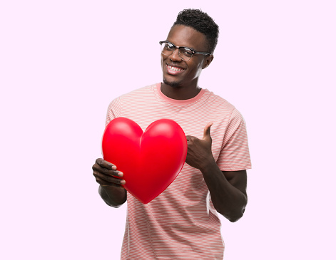 Young african american man holding red heart happy with big smile doing ok sign, thumb up with fingers, excellent sign