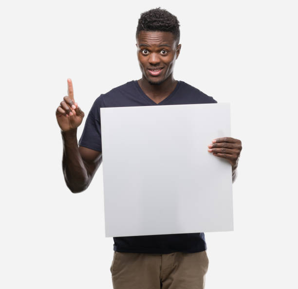 istock Young african american man holding a banner surprised with an idea or question pointing finger with happy face, number one 1042741162