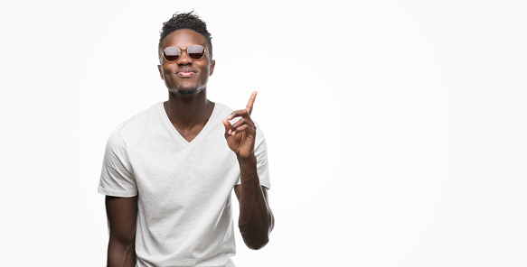 Young african american man wearing sunglasses surprised with an idea or question pointing finger with happy face, number one