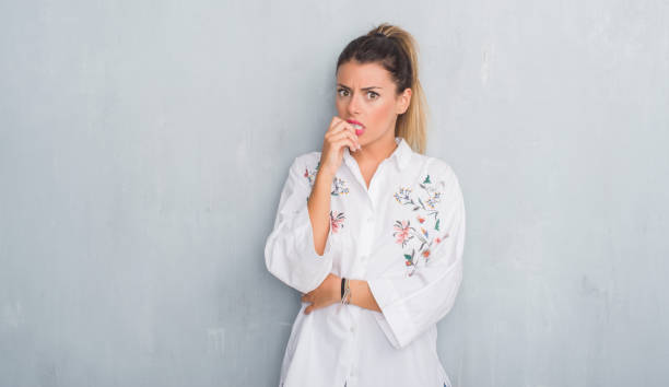 Young adult woman over grunge grey wall wearing flowers shirt looking stressed and nervous with hands on mouth biting nails. Anxiety problem. Young adult woman over grunge grey wall wearing flowers shirt looking stressed and nervous with hands on mouth biting nails. Anxiety problem. nail biting stock pictures, royalty-free photos & images