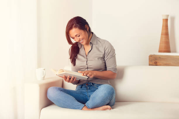 istock Woman reading a book on couch at home 1042756600