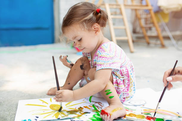 cute little caucasian girl enjoying painting at the backyard with paper, water colour and art brush. selective focus - brincar ilustrações imagens e fotografias de stock