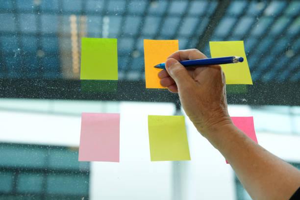 istock hand write on adhesive notes on glass wall. Sticky note paper reminder schedule for discussing creative idea & business brainstorming 1042759152