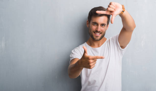 istock Handsome young man over grey grunge wall smiling making frame with hands and fingers with happy face. Creativity and photography concept. 1042766172