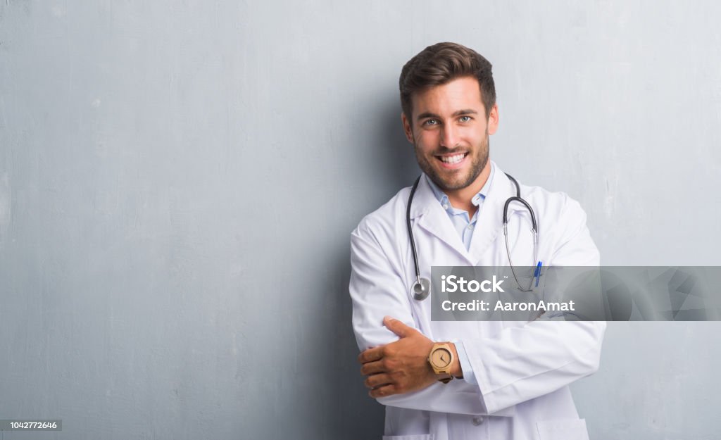 灰色グランジ壁の幸せそうな顔が笑みを浮かべてカメラを見て組んだ腕を男はハンサムな若い医者。肯定的な人。 - 医師のロイヤリティフリーストックフォト