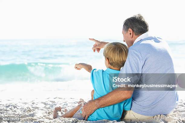 Grandfather And Grandson Sitting On Beach Stock Photo - Download Image Now - Beach, Grandparent, Multi-Generation Family