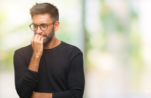 Adult hispanic man wearing glasses over isolated background looking stressed and nervous with hands on mouth biting nails. Anxiety problem.