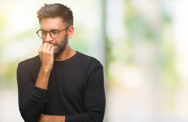 Photo of Adult hispanic man wearing glasses over isolated background looking stressed and nervous with hands on mouth biting nails. Anxiety problem.