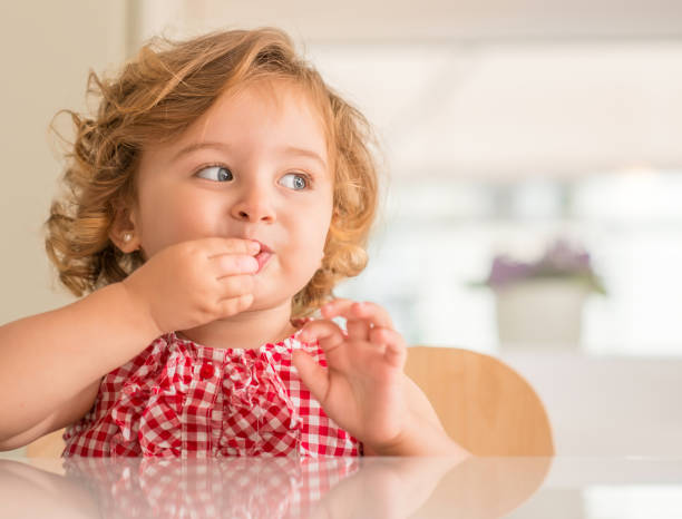Beautiful small child, cute little girl at home Beautiful blonde child with blue eyes eating candy and looking side at home. gummy candy stock pictures, royalty-free photos & images