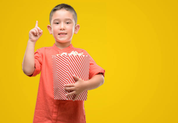 istock Dark haired little child eating popcorn surprised with an idea or question pointing finger with happy face, number one 1042793186