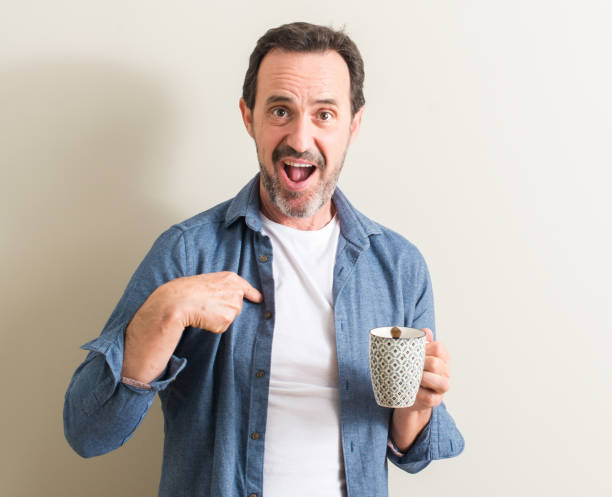 istock Senior man drinking coffee in a mug with surprise face pointing finger to himself 1042799408