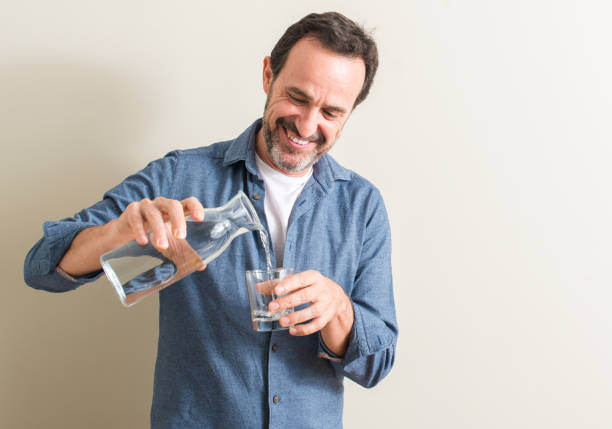 senior woman trinkwasser in ein glas mit ein glückliches gesicht stehen und lächeln mit einem zuversichtlich lächeln zeigt zähne - toothy smile relaxation white healthcare and medicine stock-fotos und bilder