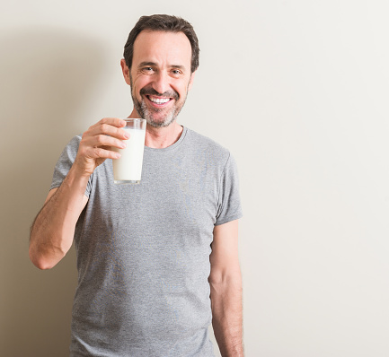 Senior man drinking a glass of milk with a happy face standing and smiling with a confident smile showing teeth