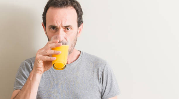istock Senior man drinking orange juice in a glass with a confident expression on smart face thinking serious 1042800154