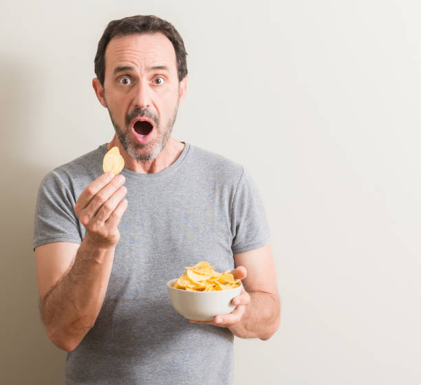 istock Senior man eating potato chips scared in shock with a surprise face, afraid and excited with fear expression 1042800224