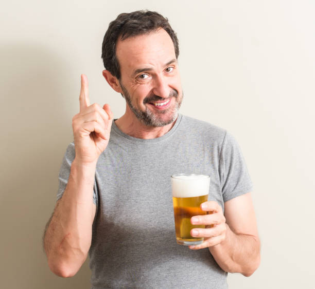 istock Senior man drinking beer surprised with an idea or question pointing finger with happy face, number one 1042800234
