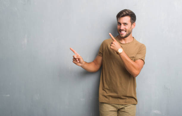istock Handsome young man over grey grunge wall smiling and looking at the camera pointing with two hands and fingers to the side. 1042811554