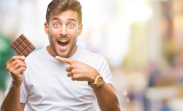 istock Young handsome man eating chocolate bar over isolated background very happy pointing with hand and finger 1042816218