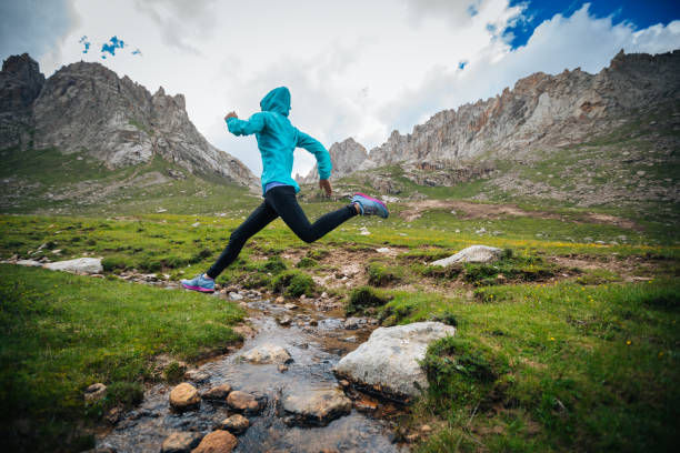 istock Woman trail runner jumping over samll river on beautiful mountains 1042819412