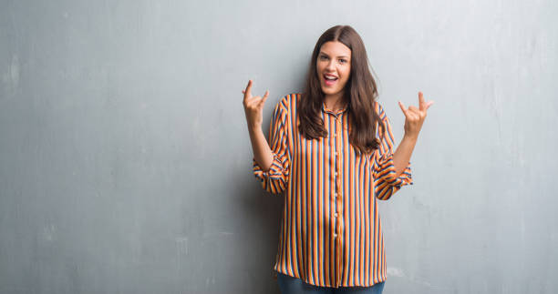 istock Young brunette woman over grunge grey wall shouting with crazy expression doing rock symbol with hands up. Music star. Heavy concept. 1042819912