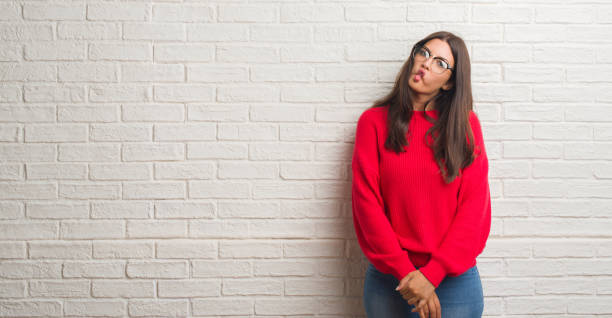 istock Young brunette woman standing over white brick wall making fish face with lips, crazy and comical gesture. Funny expression. 1042824948