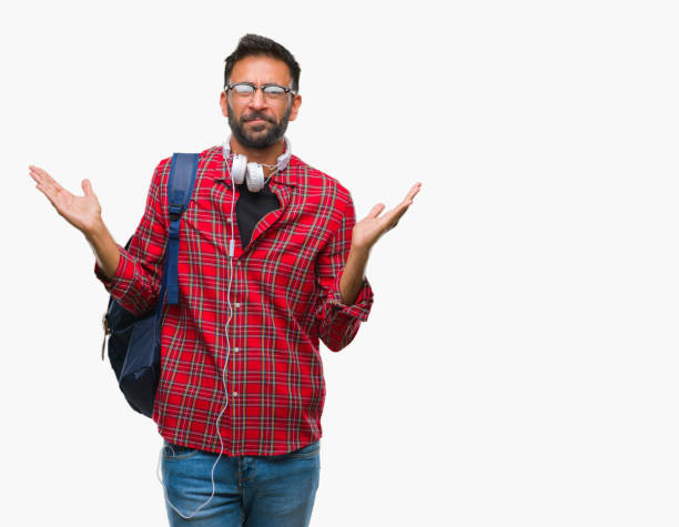 adult hispanic student man wearing headphones and backpack over isolated background clueless and confused expression with arms and hands raised. doubt concept. - head and shoulders audio imagens e fotografias de stock