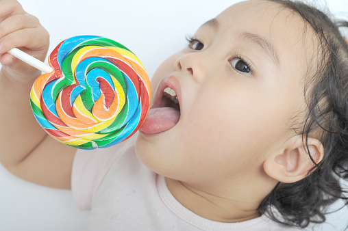 little child happily licking a colorful candy stick.