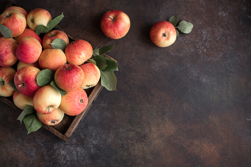Red apples in wooden box. Organic red apples with leaves on rustic background, copy space.