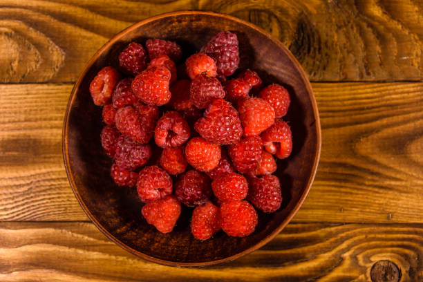 istock Ceramic plate with ripe raspberries on wooden table. Top view 1042894276