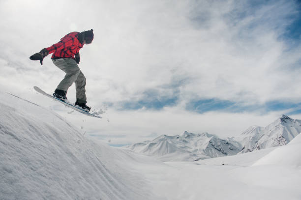 istock man is jumping on a snowboard against a snow-capped mountain peaks 1042897572