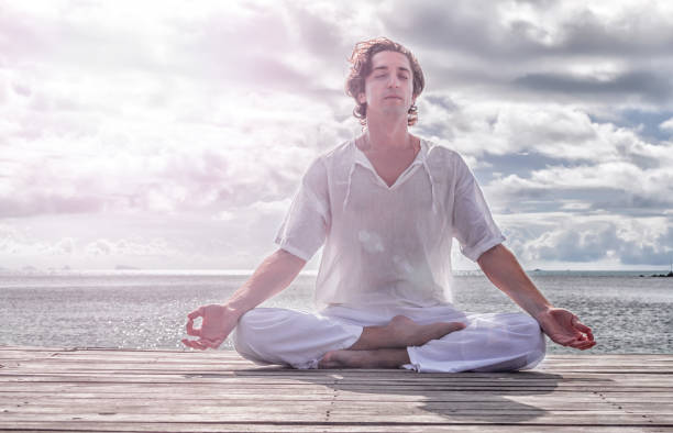 istock Young man meditating with closed eyes on the beach, clouds in the background 1042915012