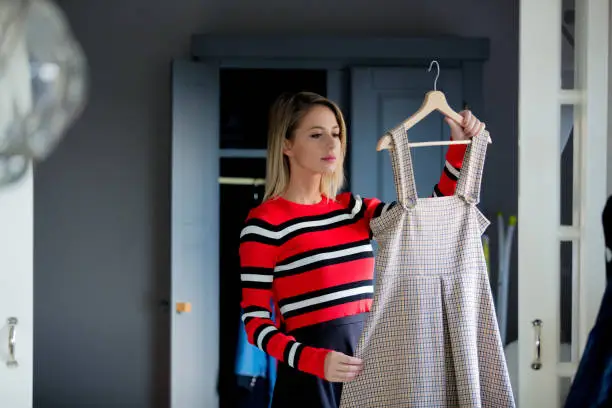 Photo of Young girl choose a dress at home near wardrobe