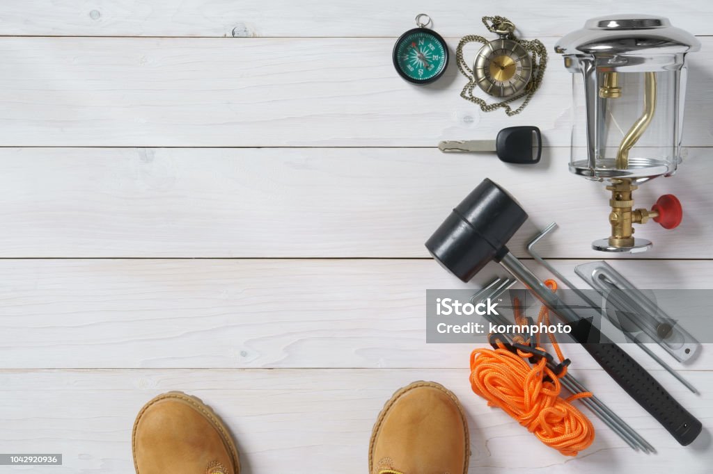 travel item frame for holiday relax and adventure with knife, boots, lantern, car key, compass, clock, rubber hammer, anchor and tent rope on white vintage wood floor or table top view for background Adventure Stock Photo