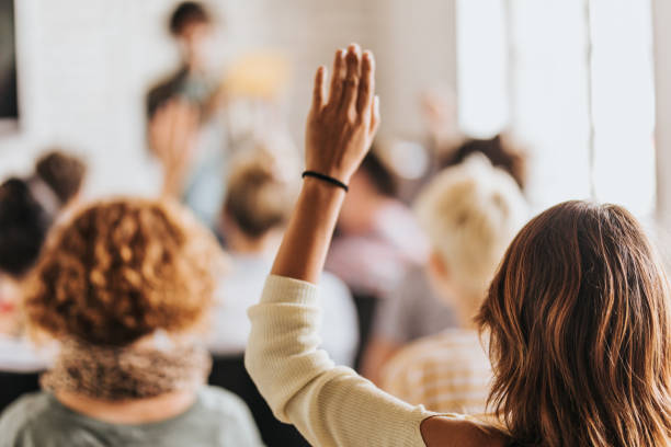 vista posterior de una mujer levantando su brazo en un seminario. - alzar la mano fotografías e imágenes de stock