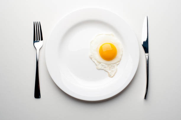 istock Scrambled eggs on a white plate with a fork and a knife. Green onion near the plate 1042932698
