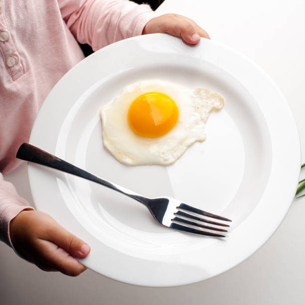 istock Children's hands hold a white plate with an egg, a fork and a knife. 1042932770