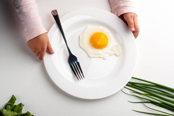 istock Children's hands hold a white plate with an egg, a fork and a knife. 1042932776