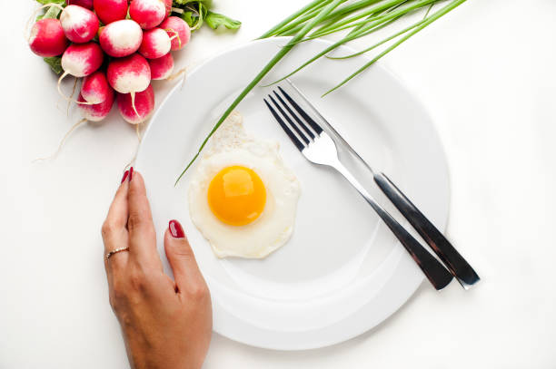 istock Women's hands hold a white plate with an egg, a fork and a knife 1042932790
