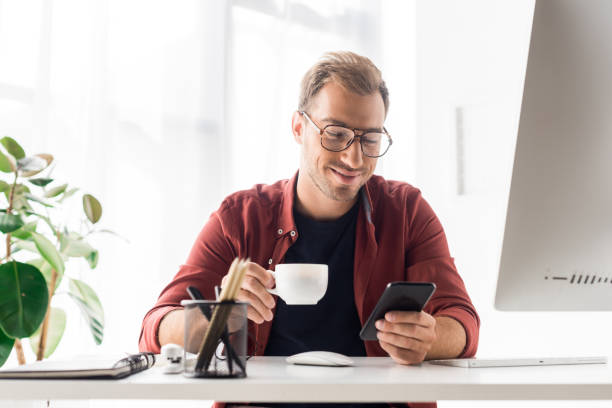 istock businessman with cup of coffee using smartphone in modern office 1042932988