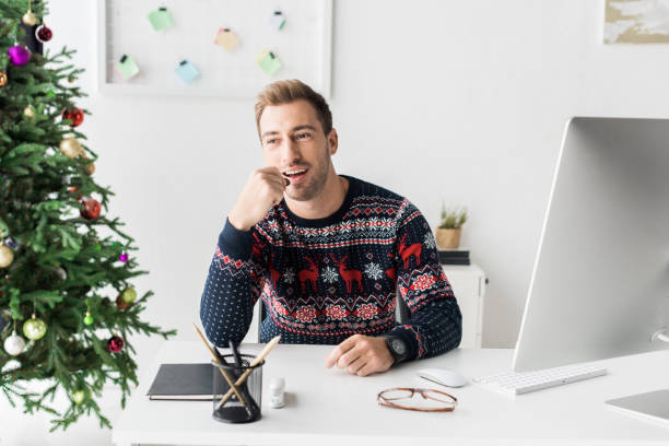 istock businessman in christmas sweater sitting by table in modern office 1042933064