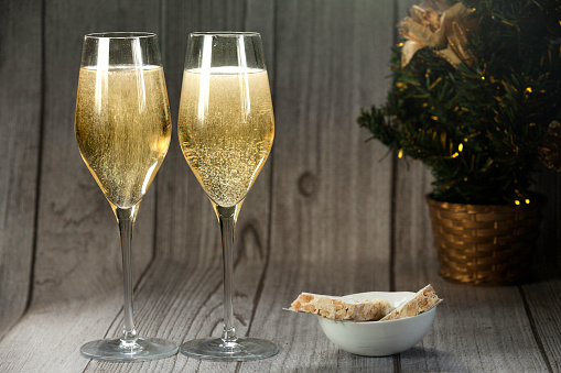 Two champagne glasses, almond nougat and christmas tree on wood background