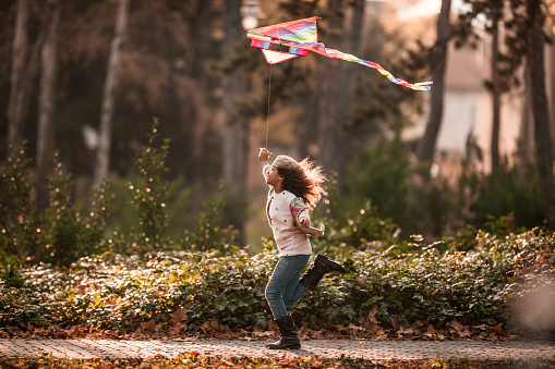 Playful black girl having fun while running with a kite in autumn day at the park.