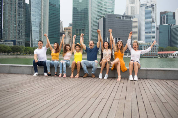 istock Cheerful friends sitting on ground arms raised 1042948338