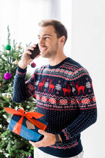 istock man in christmas sweater with gift box talking on smartphone 1042948764