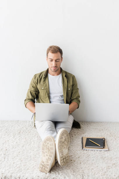 istock casual man using laptop on beige rug, remote work 1042948790