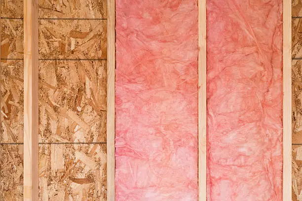 Close-up of strips of pink fiberglass insulation in a wall of a new building. Horizontal shot.