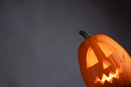 Halloween pumpkin head jack o lantern with candle inside on gray background