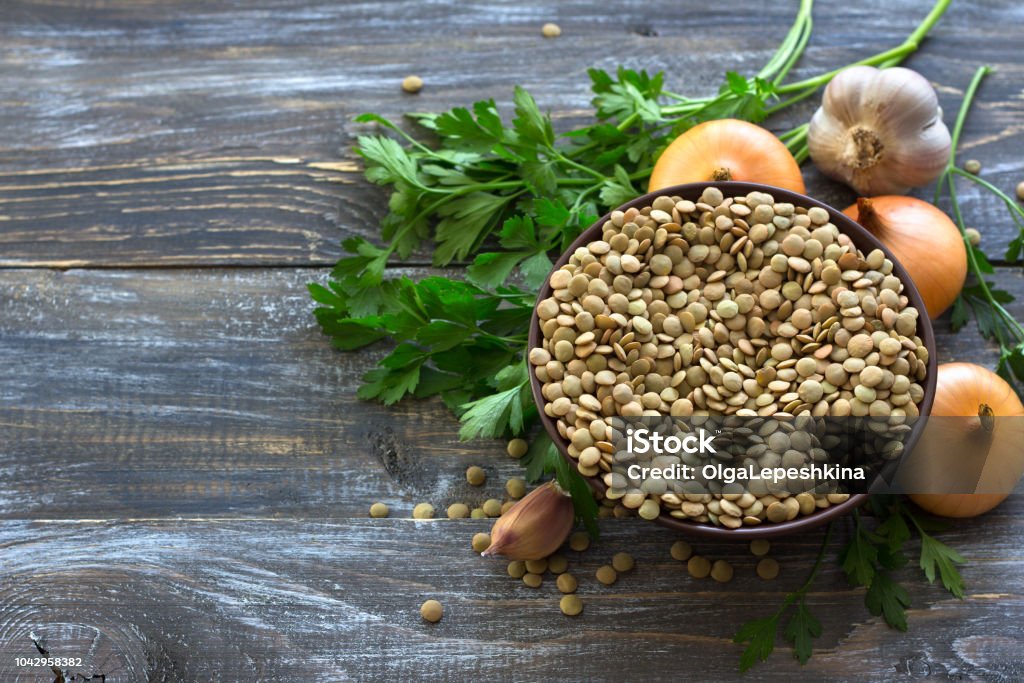 Lentils with onion, garlic and parsley on a wooden table Lentils with onion, garlic and parsley on a wooden table for a delicious vegan dish, rustic style, selective focus, horizontal Lentil Stock Photo